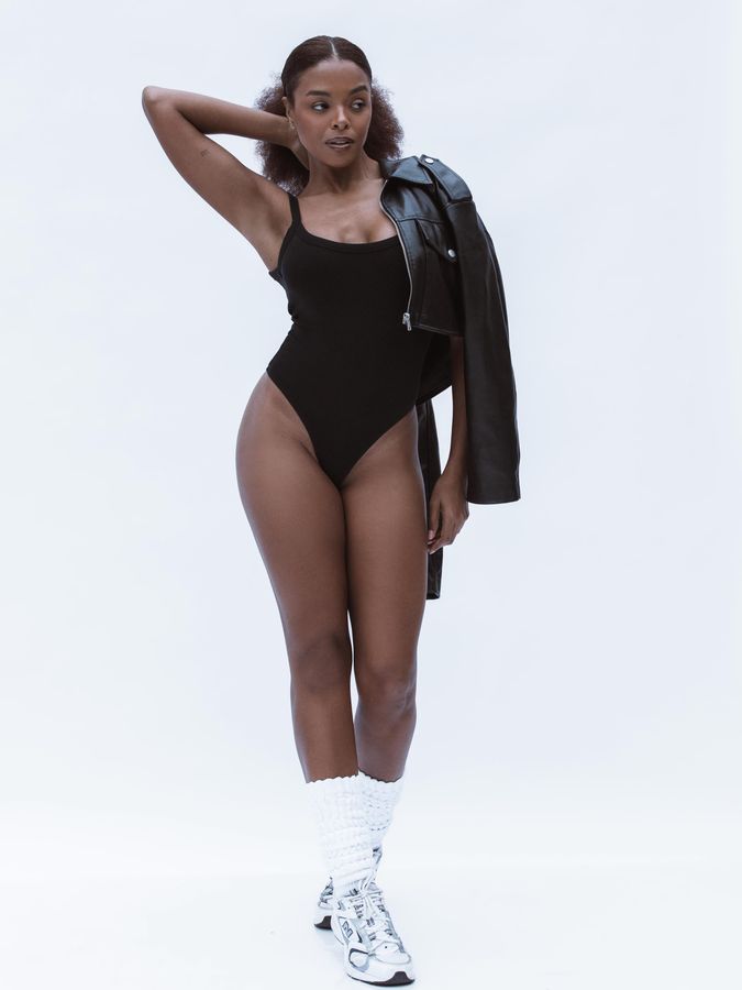 Modelo em body preto e jaqueta de couro em pose de campanha, fundo branco