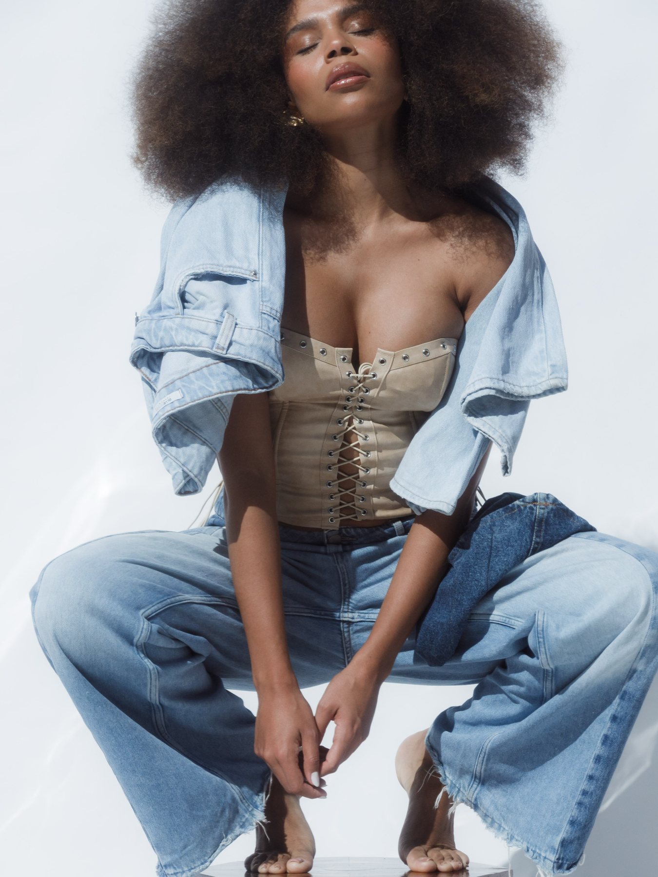 Modelo em jeans e corset bege fotografada no estúdio com luz natural